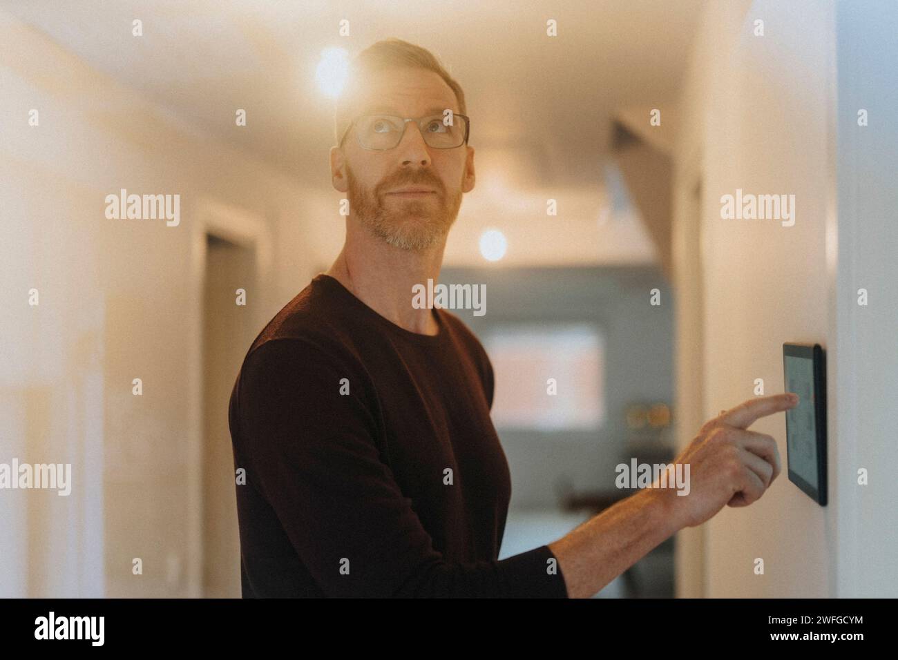Ein reifer Mann passt die Raumbeleuchtung über ein digitales Tablet an, während er im Smart Home steht Stockfoto