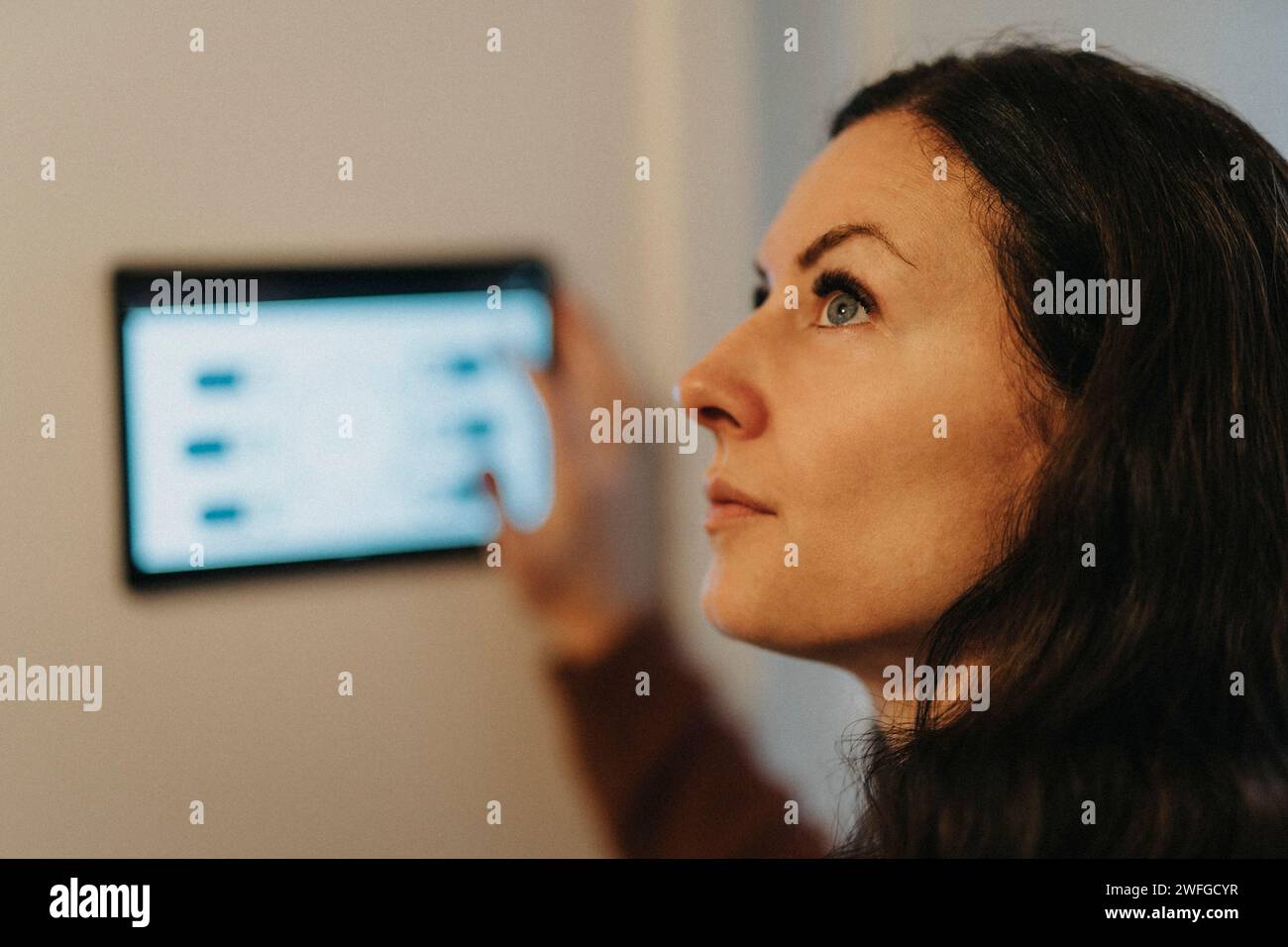 Reife Frau, die die Raumtemperatur zu Hause über ein digitales Tablet steuert Stockfoto