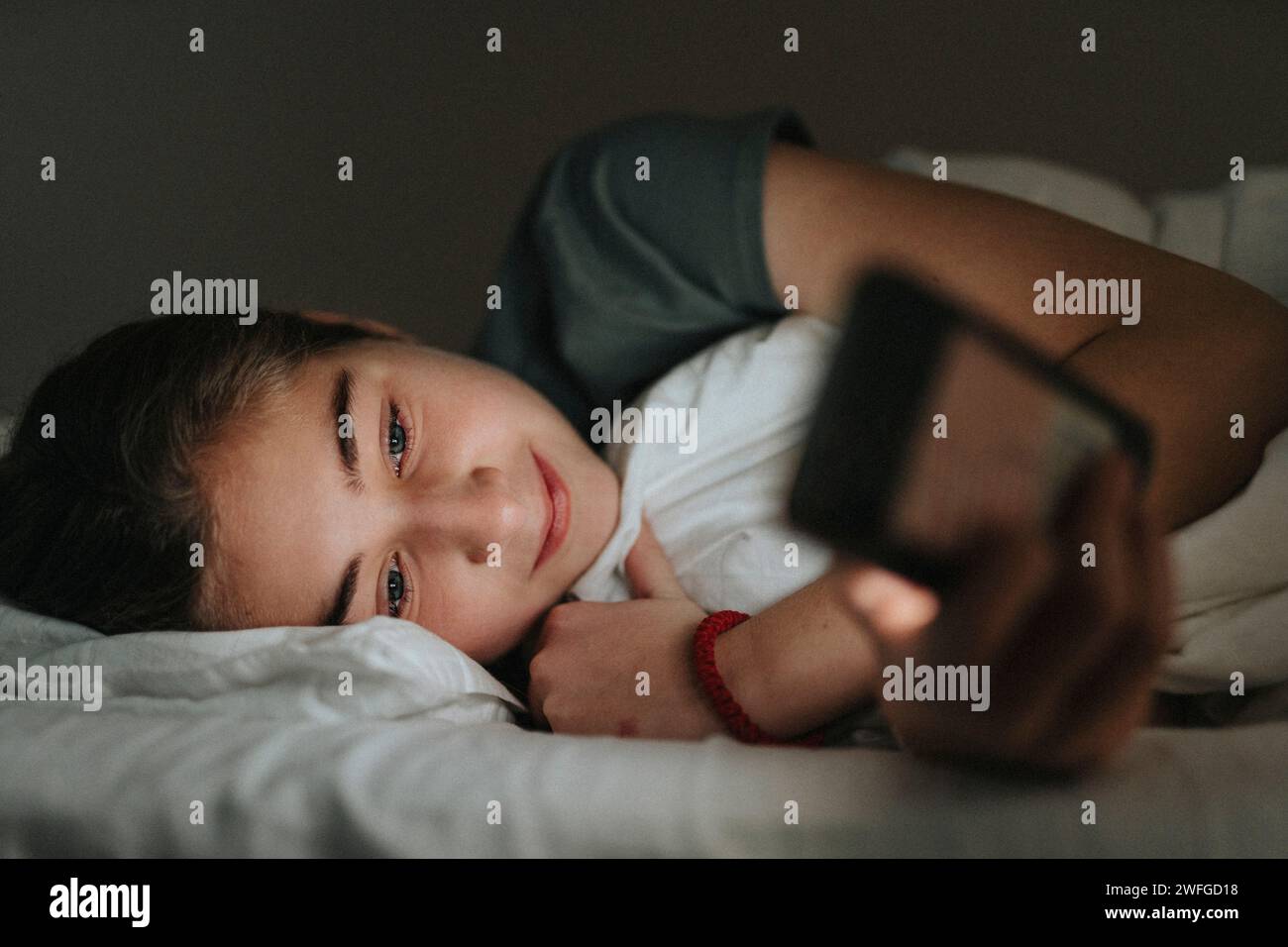 Mädchen, das ihr Smartphone benutzt, während sie im Smart Home auf dem Bett liegt Stockfoto