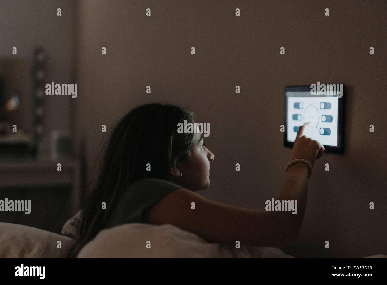 Mädchen passt die Temperatur im Schlafzimmer über ein digitales Tablet zu Hause an Stockfoto