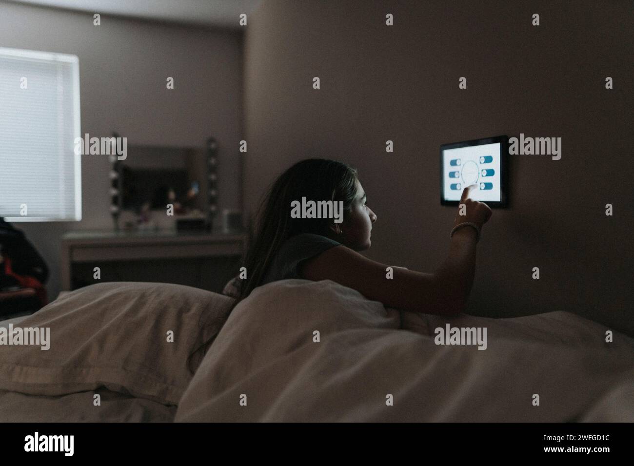 Mädchen passt die Temperatur im Schlafzimmer über ein digitales Tablet in einem modernen Zuhause an Stockfoto