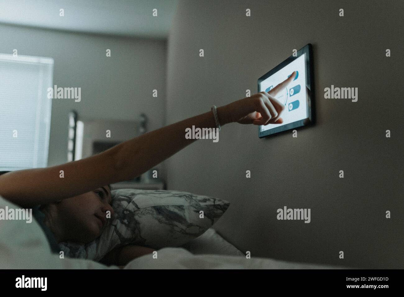 Mädchen, das die Temperatur im Schlafzimmer über ein digitales Tablet im Smart Home steuert Stockfoto