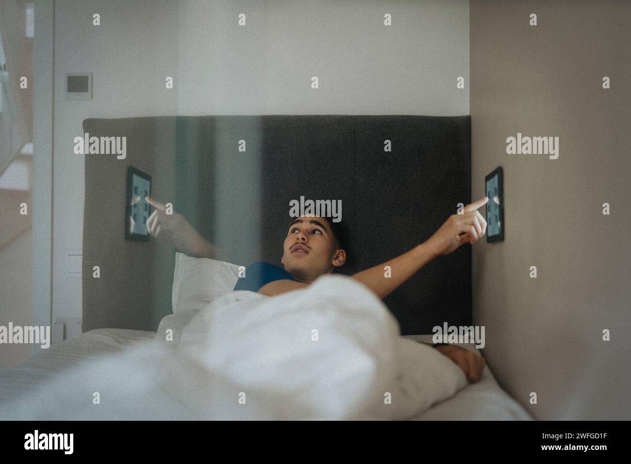 Junge passt die Temperatur im Schlafzimmer über ein digitales Tablet in einem modernen Zuhause an Stockfoto