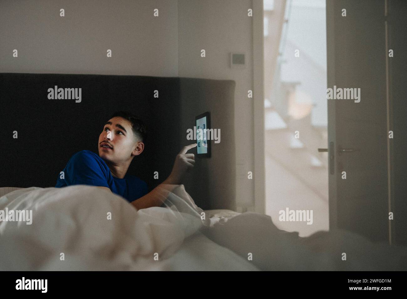 Junge, der die Temperatur des Schlafzimmers über ein digitales Tablet in einem modernen Zuhause steuert Stockfoto