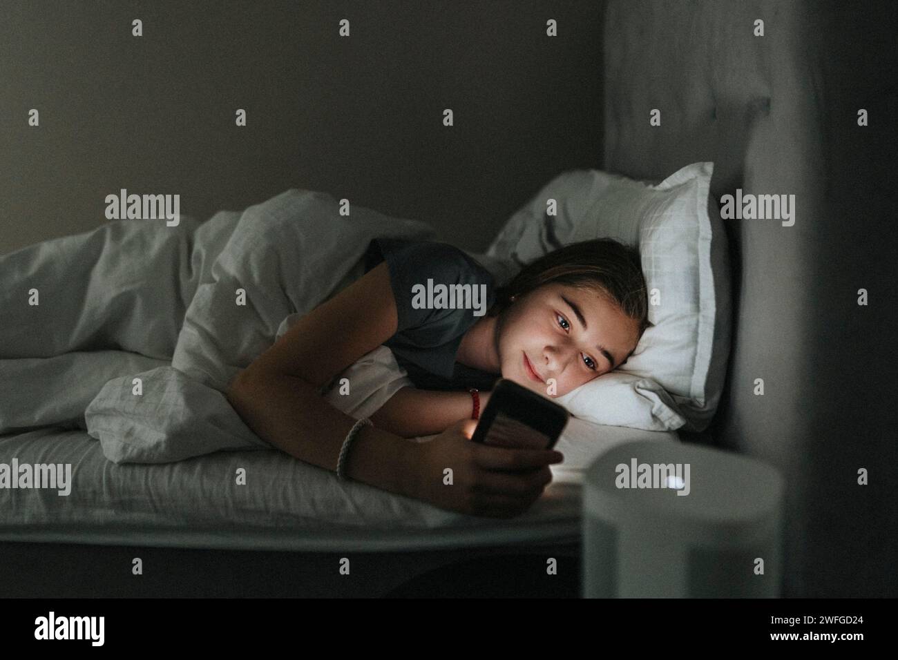 Vorpubertägliches Mädchen, das ein Smartphone benutzt, während es im Schlafzimmer eines modernen Heims auf dem Bett liegt Stockfoto