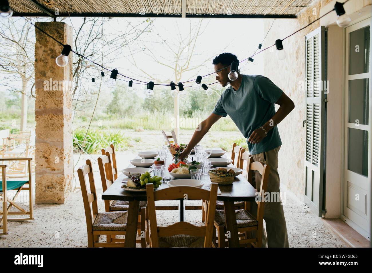 Junger Mann, der einen Esstisch für eine Dinnerparty auf der Terrasse legt Stockfoto
