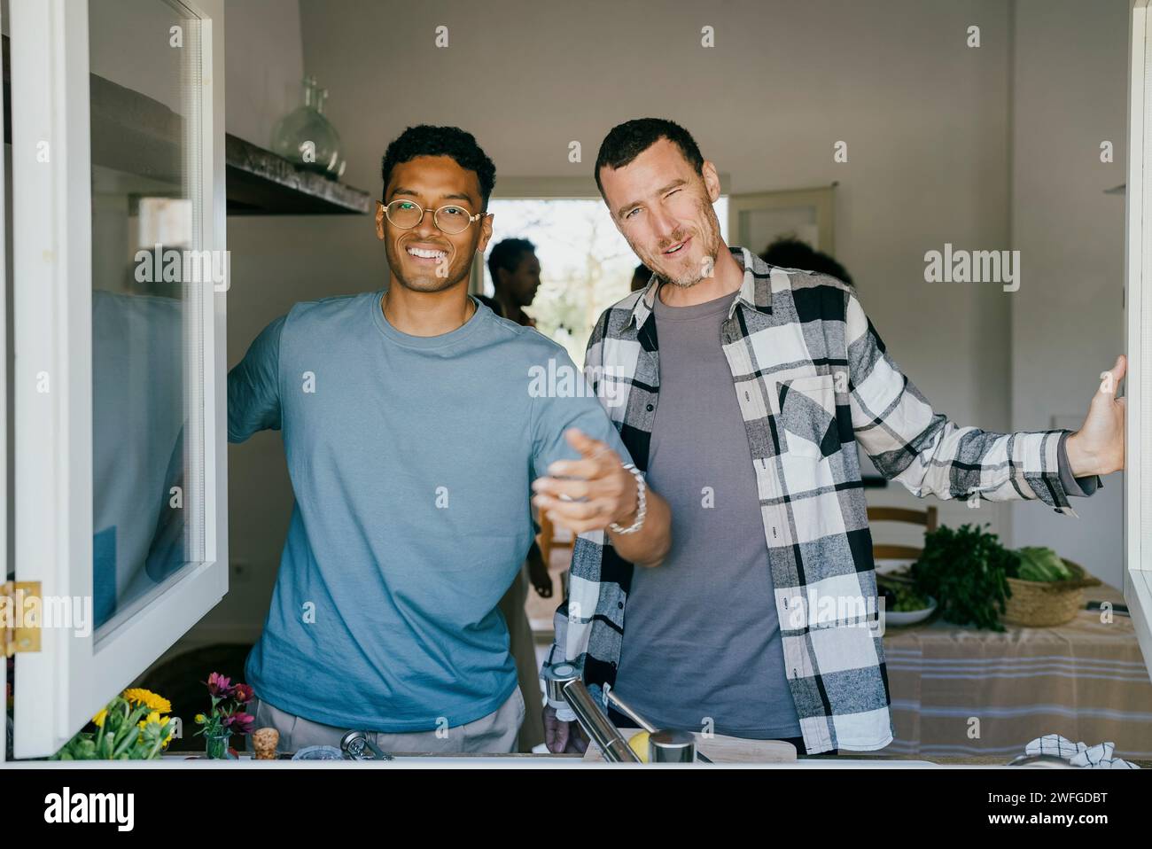 Porträt lächelnder männlicher Freunde, die in der Küche stehen, durch das Fenster gesehen Stockfoto