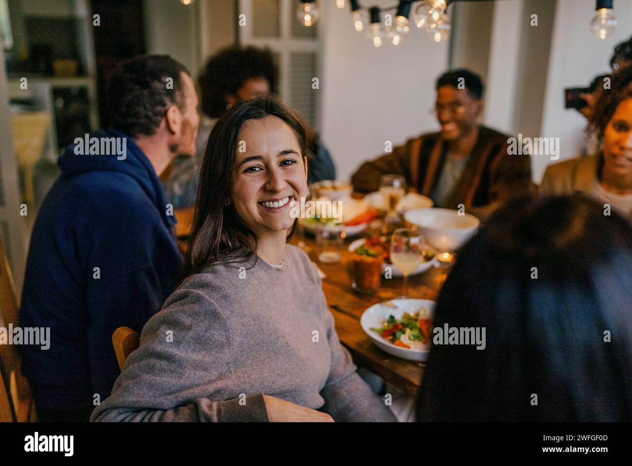 Porträt einer lächelnden jungen Frau, die mit Freunden am Esstisch sitzt Stockfoto