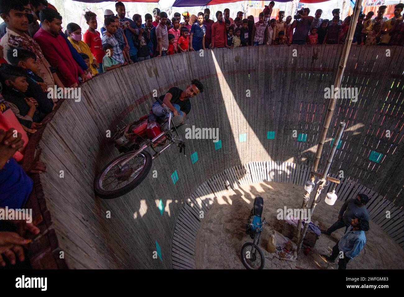 Dhaka, Khulna, Bangladesch. Januar 31, 2024. Waghalsige Autofahrer unterhalten die Zuschauer, indem sie gefährlich Motorräder auf einer vertikalen „Mauer des Todes“ in Khulna, Bangladesch, fahren. Bei Geschwindigkeiten von bis zu 80 km/h fahren die Künstler ohne Schutzausrüstung, damit ihre Fahrzeuge auf der 25 Fuß hohen Holzplanke balancieren können. Die Fahrer ziehen tödliche Stunts ab, um Zuschauer zu begeistern, um zusätzliches Geld zu verdienen, während sie senkrecht an einer Wand entlang fahren. Sie führen auf, um diejenigen zu unterhalten, die einen Eintritt von 20 Pence für die Unterhaltung bezahlt haben. Bis zu 100 Zuschauer können gleichzeitig dabei zusehen, wie sie Geld anbieten Stockfoto