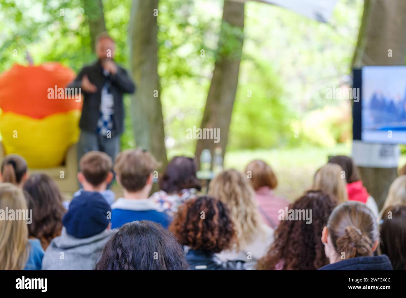Unscharfes Publikum im Freien, das mit einem Lautsprecher in einer natürlichen, parkähnlichen Umgebung in einem Workshop teilnimmt. Stockfoto