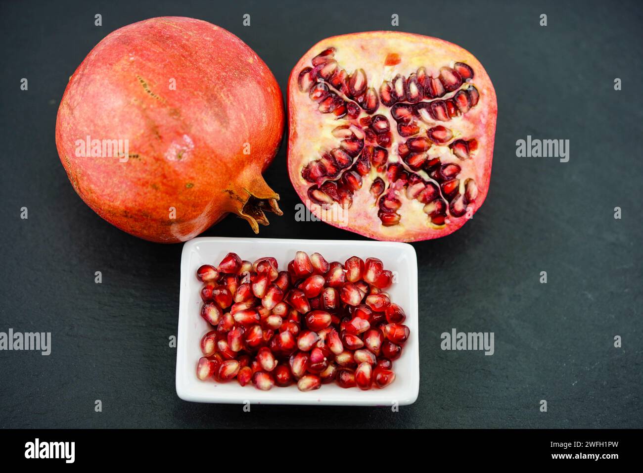 Granatapfel, anar (Punica granatum), Granatäpfel, eine Hälfte, Granatapfelkerne in einer Schüssel Stockfoto