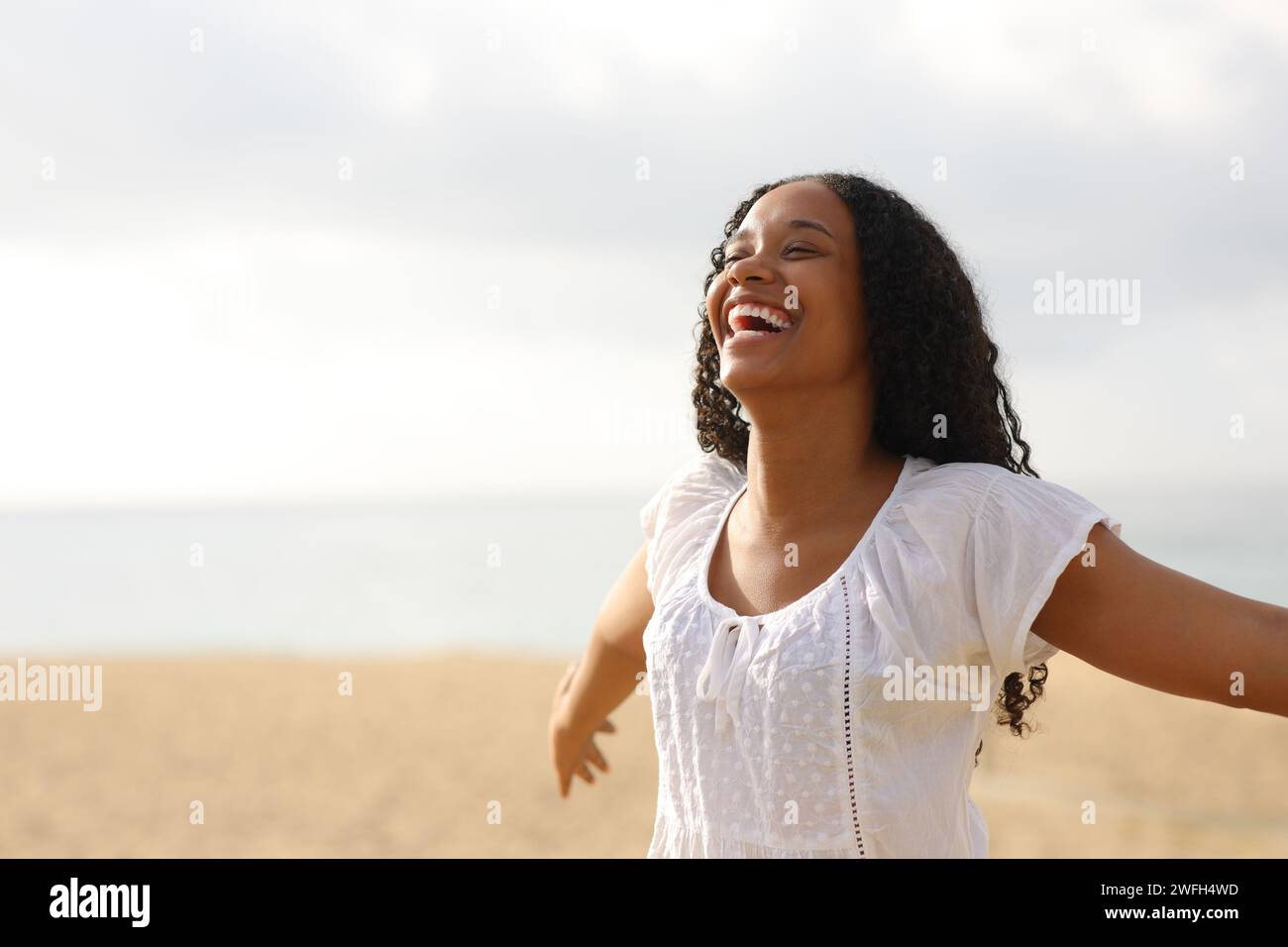 Fröhliche schwarze Frau, die Arme ausstreckt und am Strand lacht Stockfoto