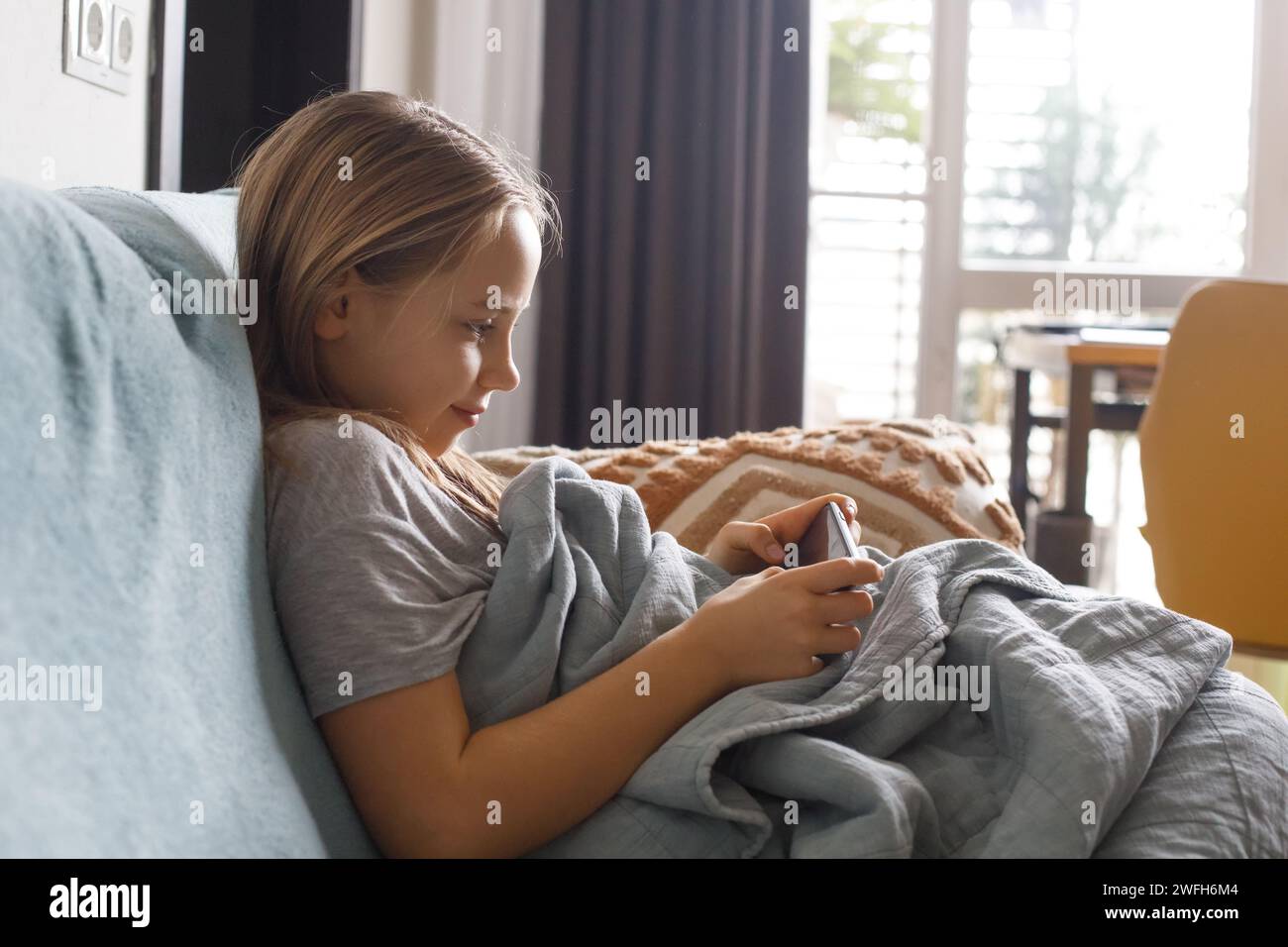 Glückliches Mädchen Kind mit Smartphone, das Videos ansieht oder zu Hause spielt. Freizeit, Kinder, Technik, Internetkommunikation und Menschenkonzept. Stockfoto