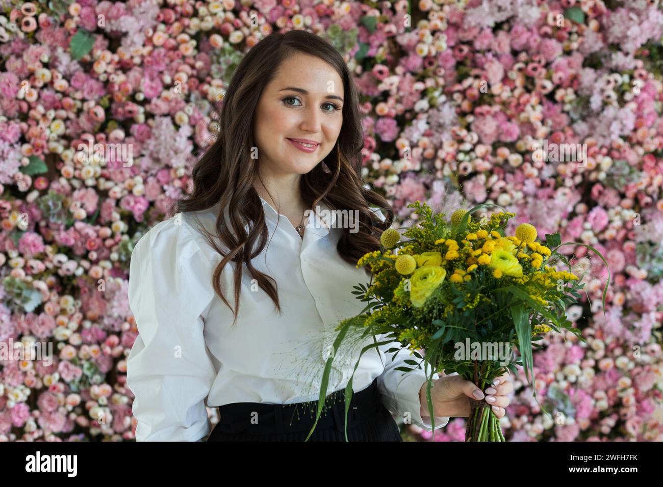 Lächelnde Dame mit gelbem Blumenstrauß vor blühendem Hintergrund. Wunderschönes Frauenporträt Stockfoto