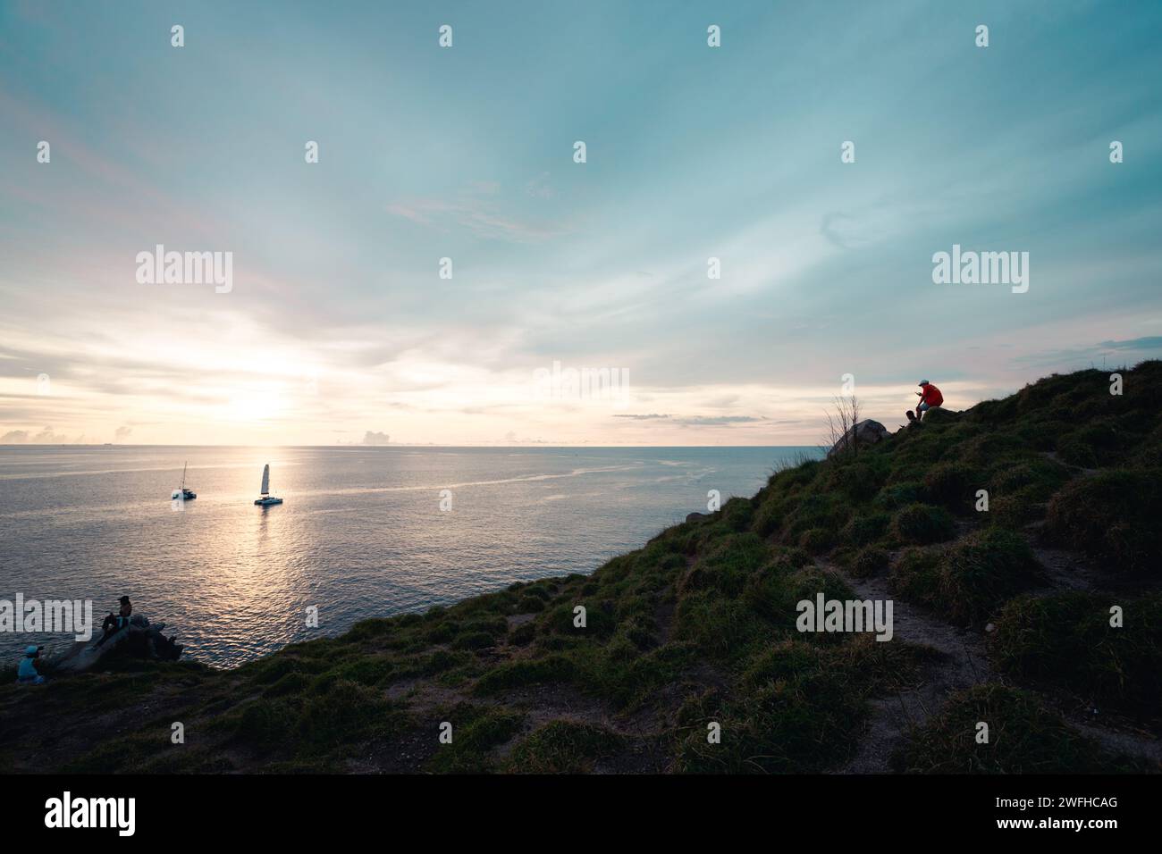 Die Menschen auf dem Hügel genießen den goldenen Sonnenuntergang mit Segelbooten über dem Meer Stockfoto