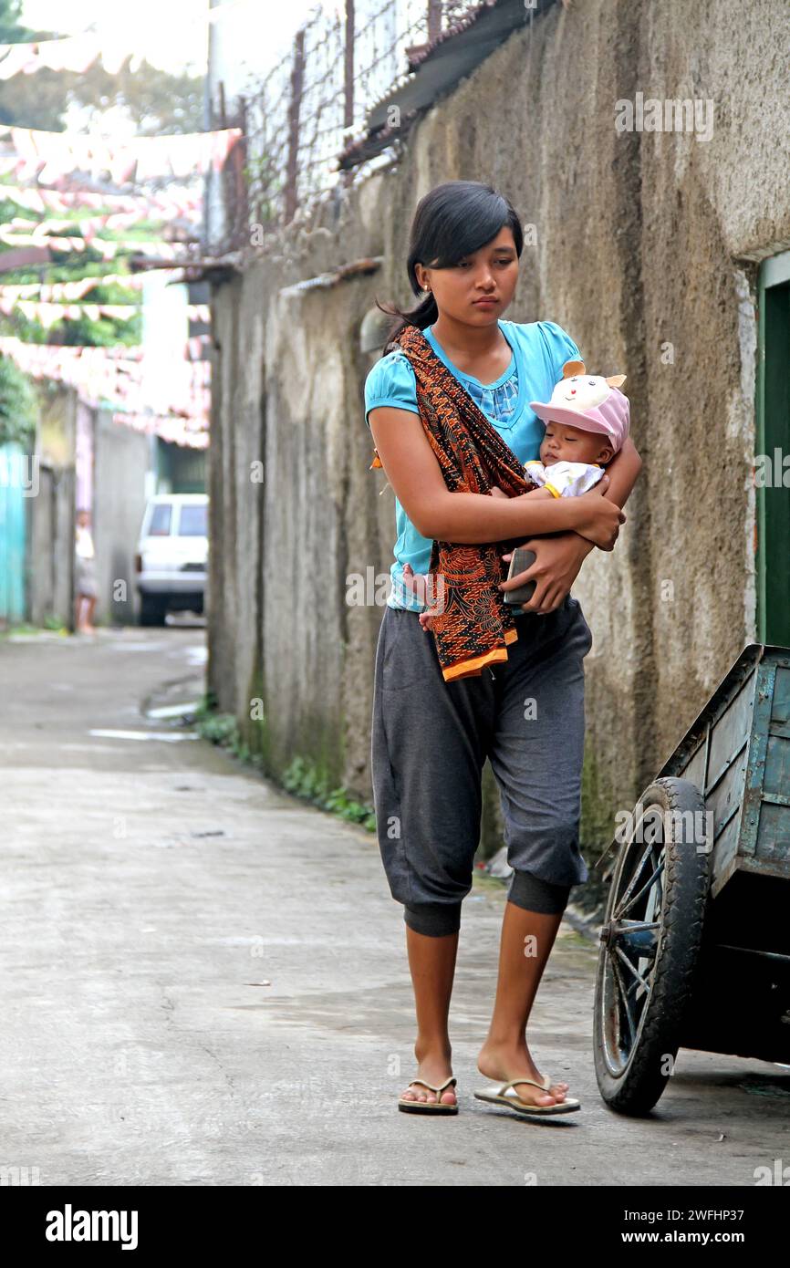 Eine junge Frau, die ein Baby in einer Seitenstraße in Bandung, West-Java, Indonesien trägt Stockfoto