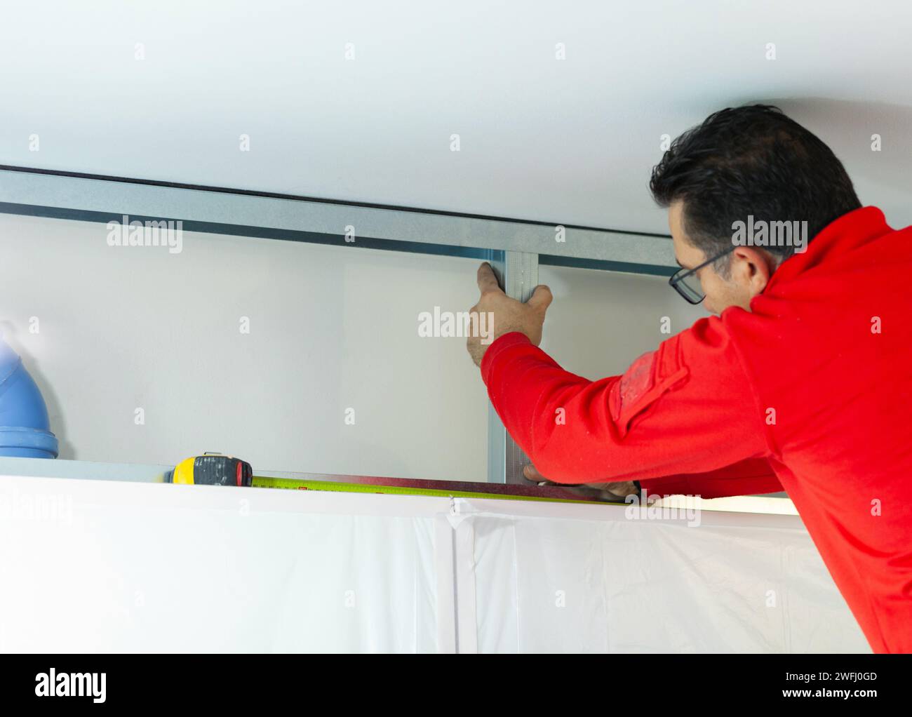 Ein Arbeiter aus Gipskarton installiert eine Gipskartonwand an den Küchenschränken, um das Absaugrohr der Haube abzudecken. Stockfoto