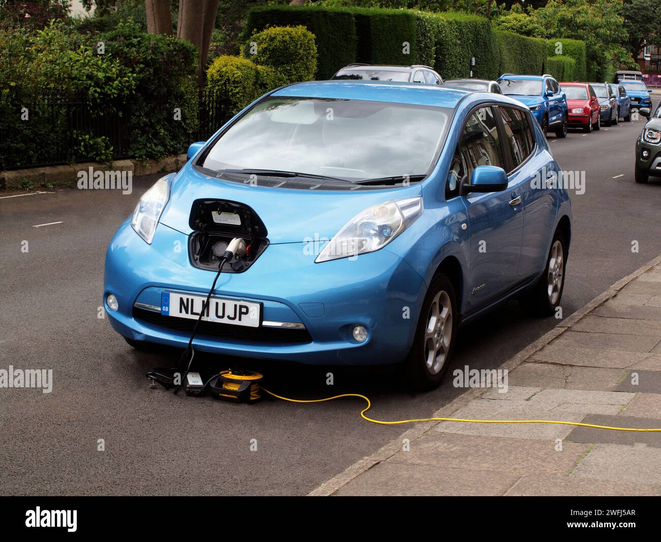 Ein „Blue Nissan Leaf Limousine Car“, bei dem die Batterieeinheit des Fahrzeugs von der Hausstromversorgung des Besitzers auf der Straße aufgeladen wird. Stockfoto