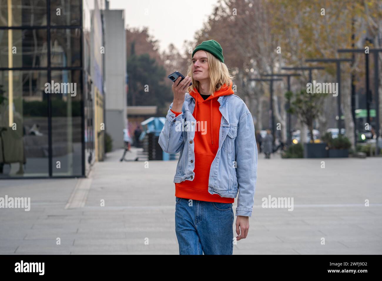 Ein sorgloser Kerl, der wie ein Tourist aussieht, ein internationaler Student, der durch die Stadt läuft und über das Handy spricht Stockfoto