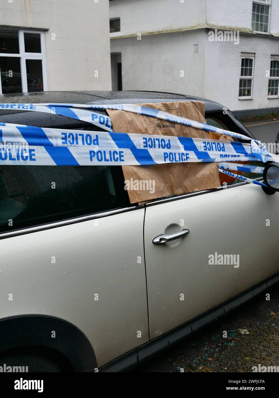 Polizei-Tatortband über einem Auto mit einem zerbrochenen, zertrümmerten Fenster aufgrund von Vandalismus oder Diebstahl. Stockfoto