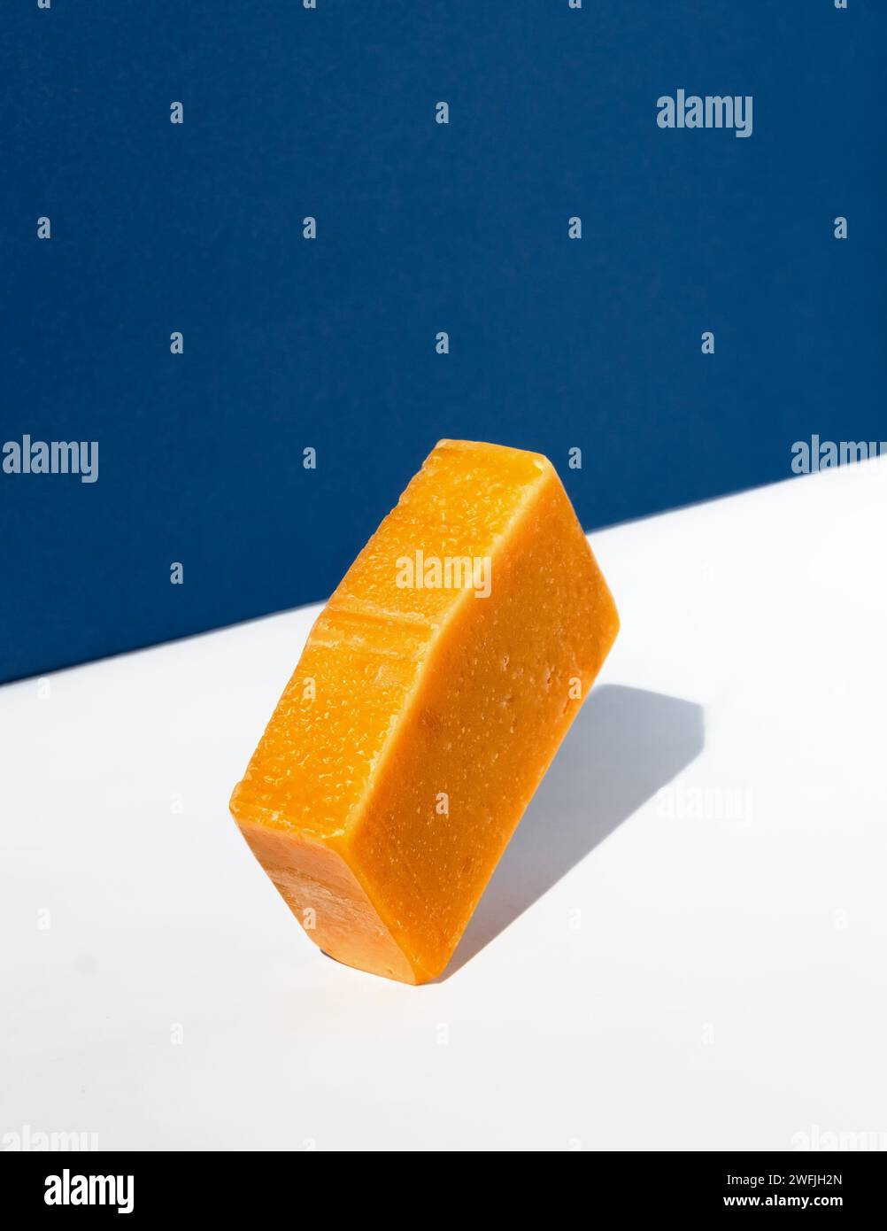 Orangefarbene Seifenleiste auf weiß-blauem Hintergrund. Kreatives Konzept der handgemachten Kosmetik aus Naturprodukten. Stockfoto