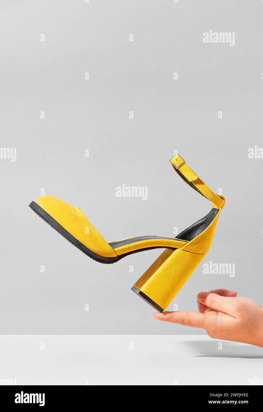 Gelber High-Heels-Wildlederschuh, der auf dem Finger der weiblichen Hand balanciert. Stockfoto