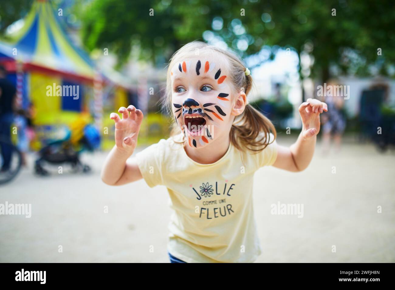 Ein kleines Vorschulmädchen mit Tigergesichtsmalerei draußen. Kinder Gesichtsmalerei. Kreative Aktivitäten für Kinder Stockfoto