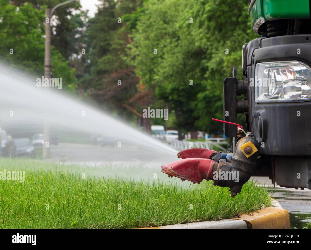 Nahaufnahme eines kommunalen Lastwagens, der den Rasen auf den Straßen bewässert. Stockfoto