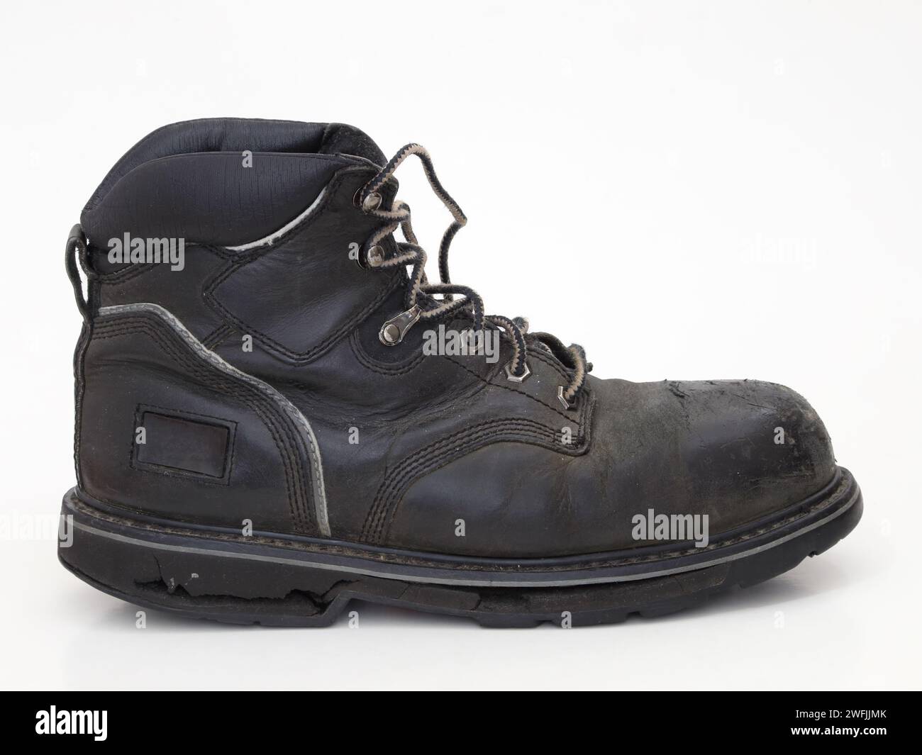 Ein alter, abgetragener, schwarzer Arbeitsstiefel aus Leder mit einer gerissenen Gummisohle wird von der Seite isoliert gegen weiß dargestellt. Stockfoto