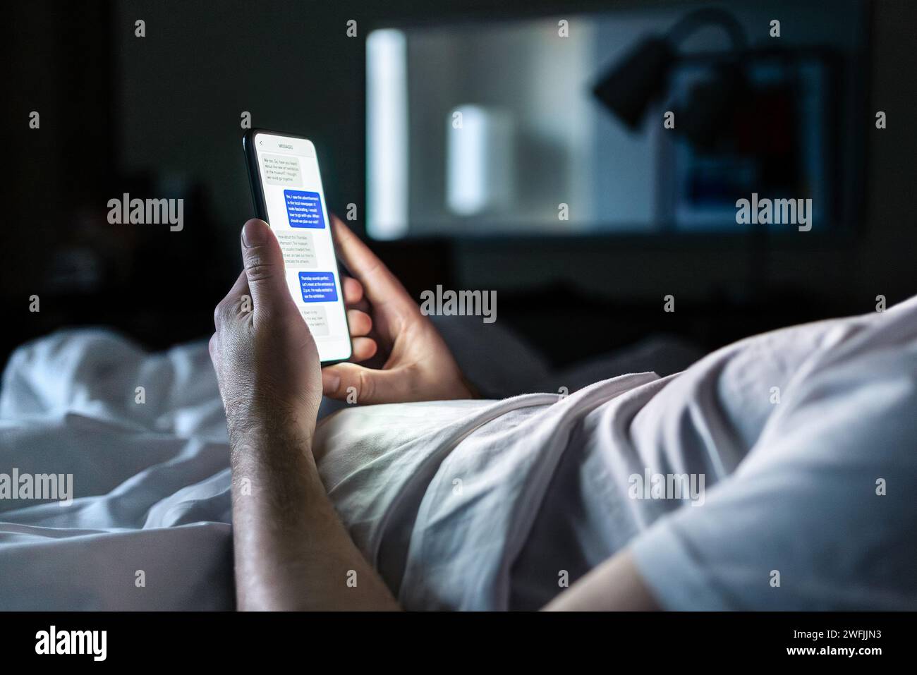 Telefon im Bett. Chat mit Textnachrichten auf dem Smartphone-Bildschirm bei Nacht. Mann im dunklen Schlafzimmer oder Hotelzimmer. Online-Dating, sms-Betrug oder geheim. Stockfoto