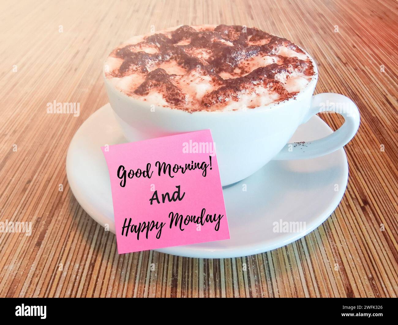 Guten Morgen und Happy monday Text geschrieben auf einem Haftnotiz mit heißer Schokolade auf einem Holztisch. Stockfoto