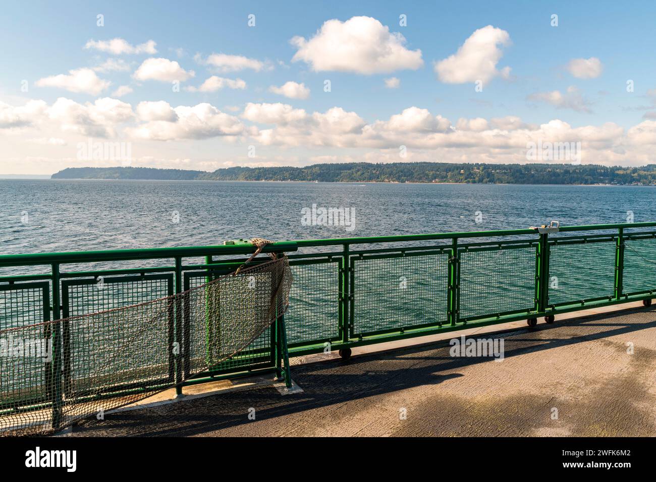 Whidbey Island befindet sich am Horizont dieses horizontalen Fotos, aufgenommen von einem Boot der Washington State Ferry, mit einem grünen Geländer, das den Rahmen teilt. Stockfoto