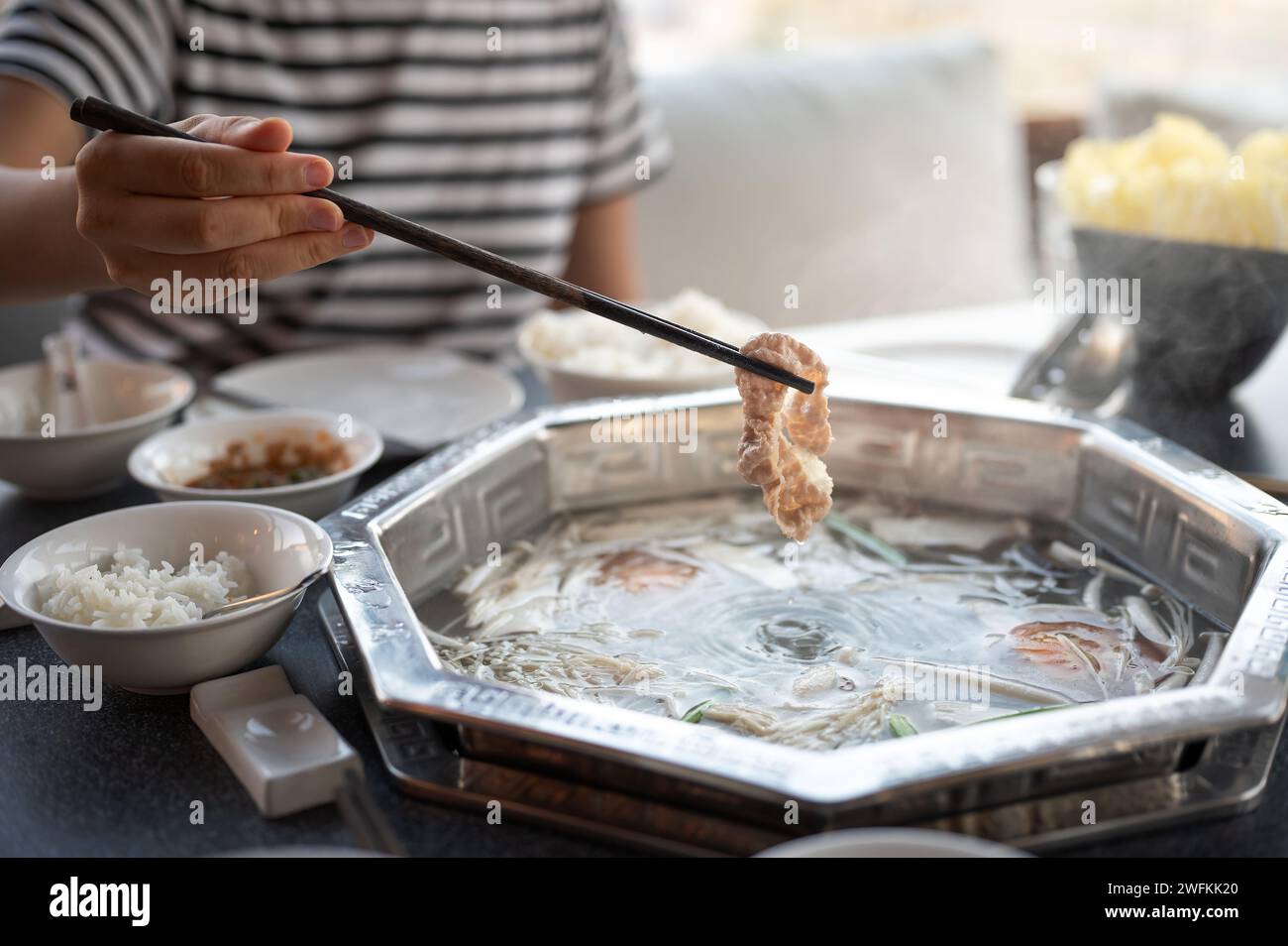 Eine Frau taucht rohes Fleisch, um in einer heißen, kochenden Suppe zu kochen. Dieses traditionelle asiatische Gericht wird mit vielen Zutaten und Fleisch zubereitet Stockfoto
