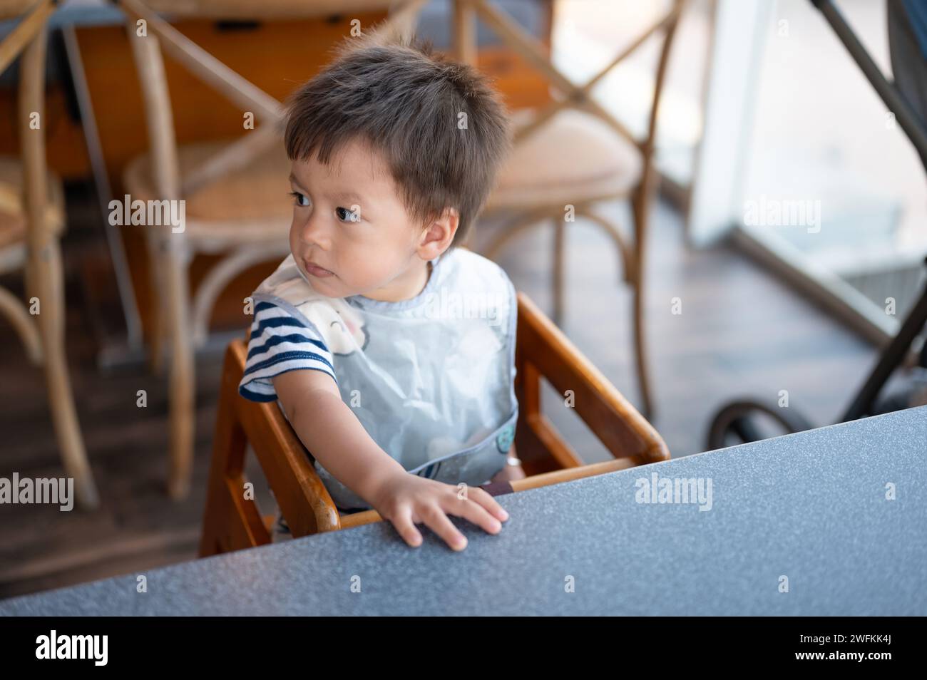 Porträt eines hungrigen Jungen in einem gestreiften T-Shirt, der in einem Restaurant in einem hohen Sessel sitzt und geduldig auf sein Mittagessen wartet Stockfoto