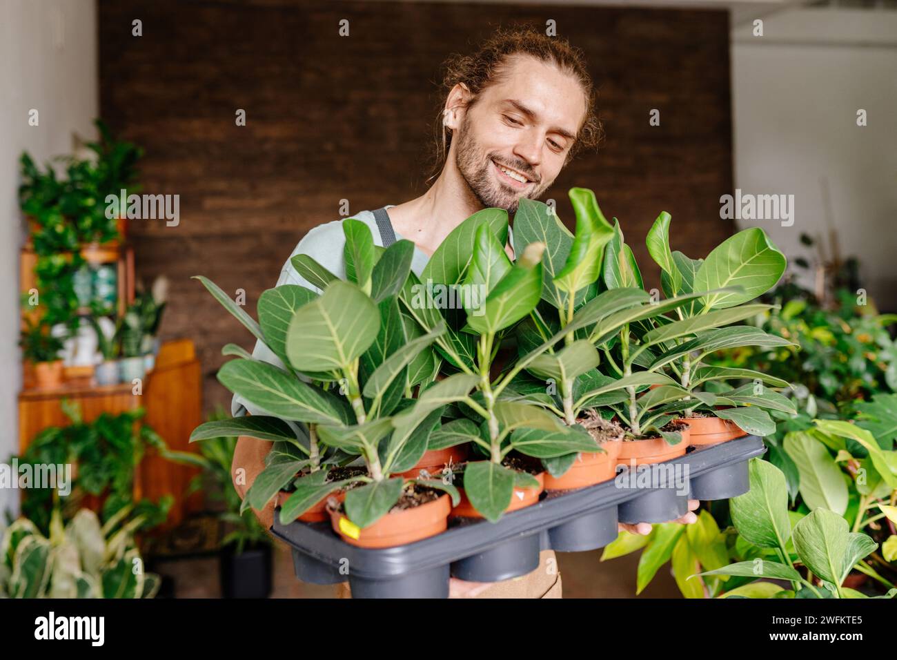 Ein Porträt eines jungen kaukasischen Gärtners mit Schürze drinnen in einem Pflanzenladen, der Blumen pflanzt. Stockfoto