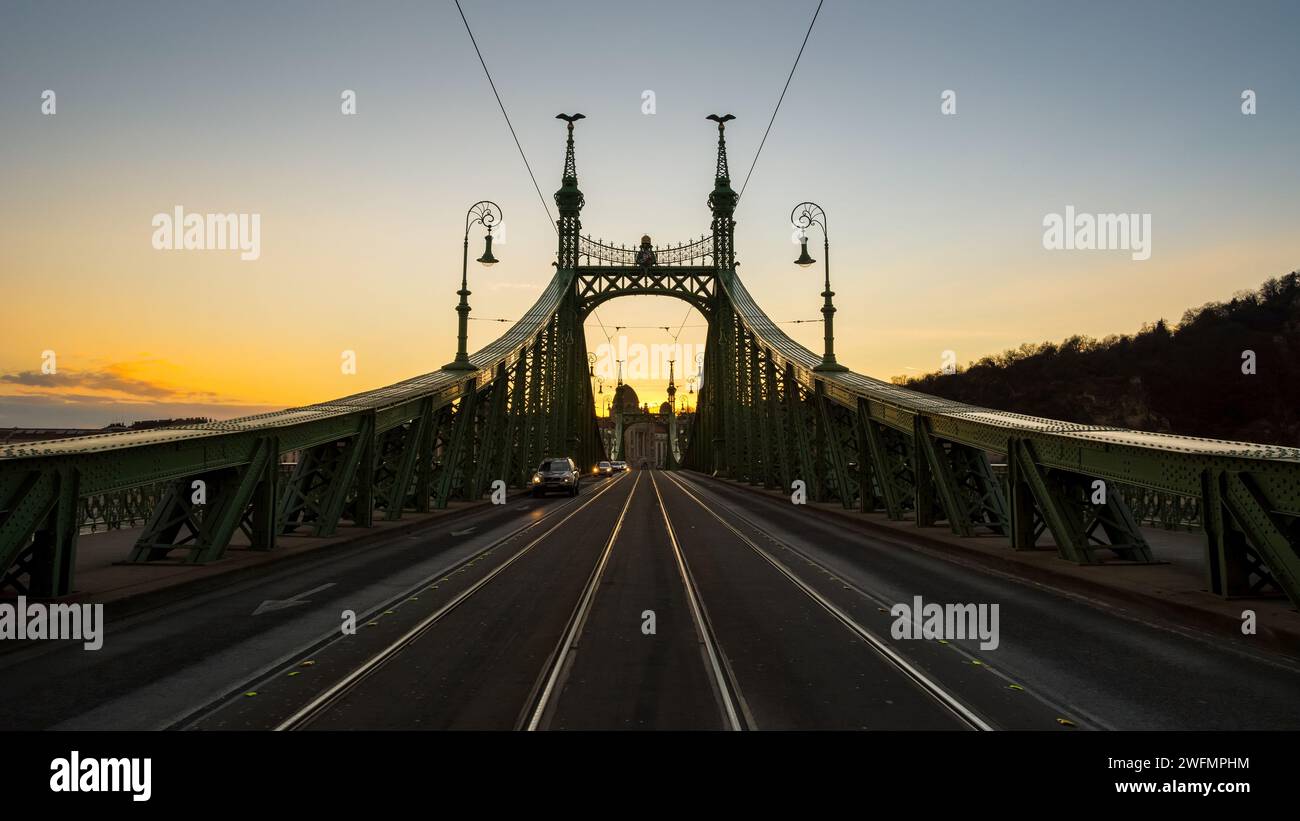 Liberty Bridge in der Abenddämmerung - symmetrische Ansicht. Blick vom Platz Fővám tér an der Brücke und am rechten Ufer der Donau. Weitwinkelsymmetrische Aufnahme der Brückenstruktur Stockfoto