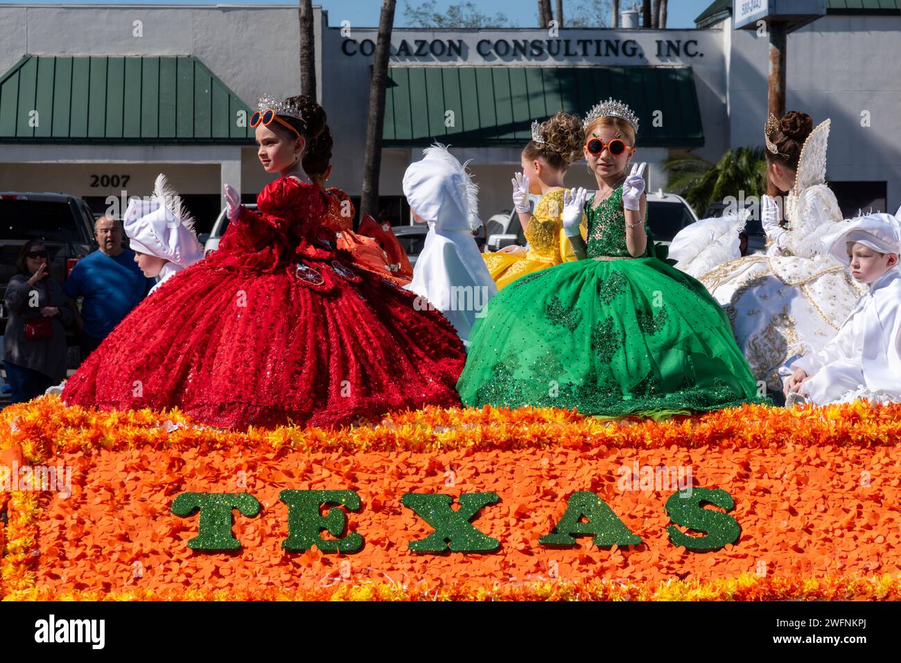 Junge Mädchen in bunten Kleidern am Rock winken der Menge bei der 92. Jährlichen Orangenparade der Texas Citrus Fiesta, Mission, TX, USA. Stockfoto