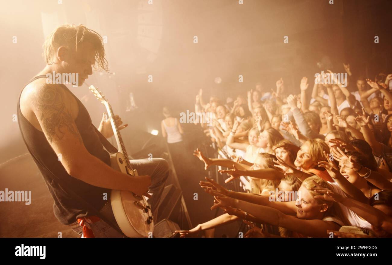 Gitarre, Musiker und Konzertbesucher auf der Bühne mit einem Mann bei der Aufführung von Rock- oder Metal-Musik. Festival, Veranstaltung und Publikum von Menschen, die feiern Stockfoto