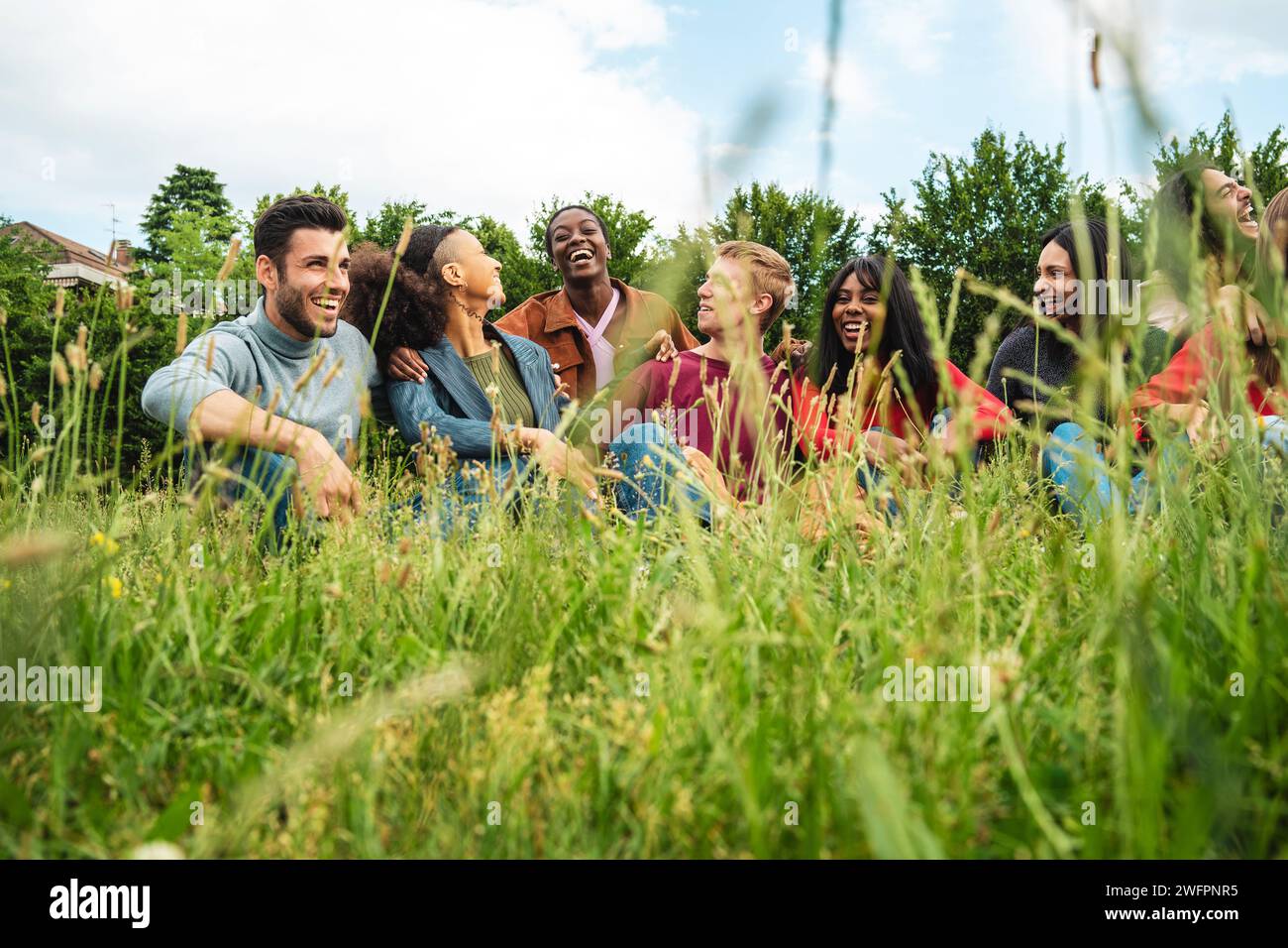 Eine vielfältige Gruppe junger Menschen lacht und genießt einen entspannenden Moment, umgeben von üppigem Grün, was die Freude an Freundschaft unterstreicht. Stockfoto