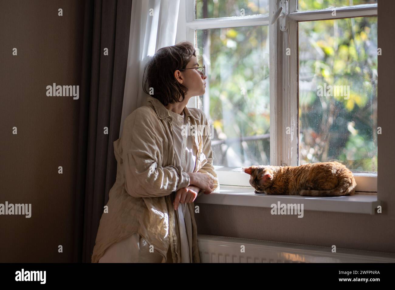 Melancholischer Haustierbesitzer, der in Depressionen auf das Fenster blickt, während er an sonnigen Sommertagen zu Hause bleibt Stockfoto