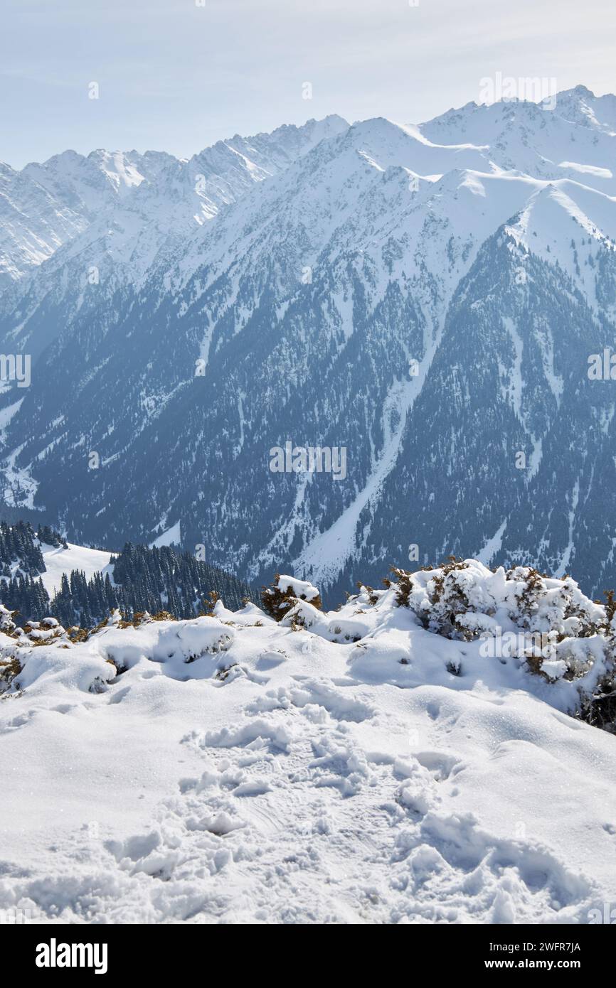 Pfad im Schnee, bis zu einem Punkt, wo Sie einen Blick auf ein Hochgebirgstal mit schneebedeckten Gipfeln haben. Skigebiet Karakol. Hintergrundbild für die Winterlandschaft. Stockfoto