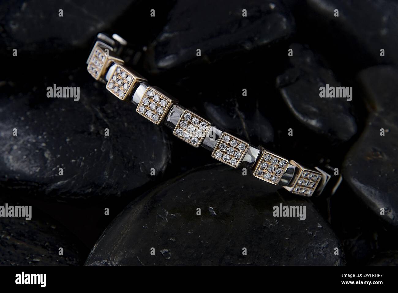 Luxuriöses Diamantarmband mit quadratischen Einstellungen, elegant auf dunklen, strukturierten Steinen, die den Glanz und die Handwerkskunst des Schmuckstücks hervorheben Stockfoto