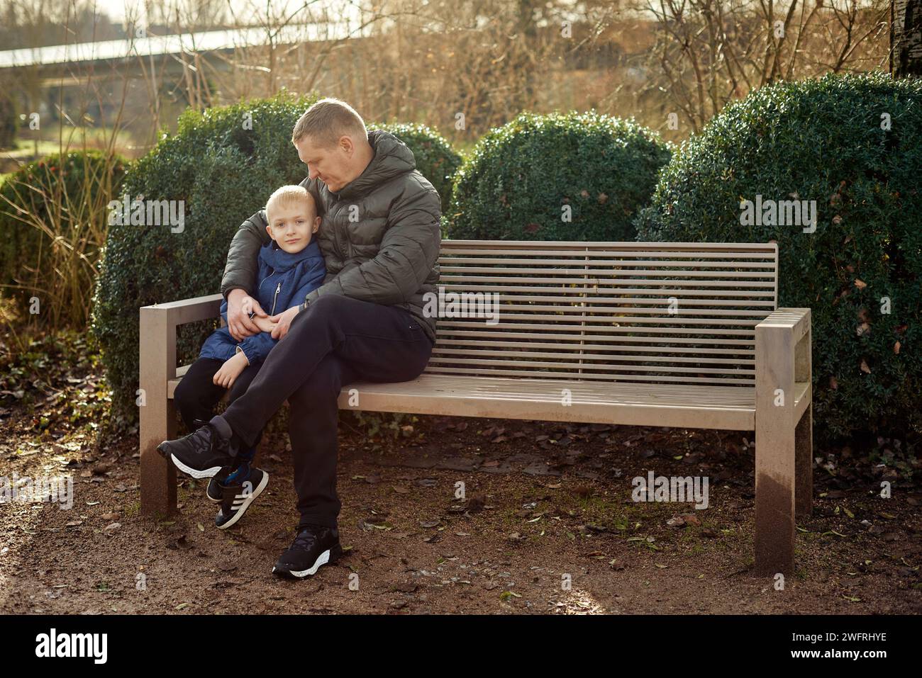 Herbstliche Familienzusammenhänge: Vater, 40 Jahre alt, und Sohn - wunderschöner 8-jähriger Junge, im Park sitzend. Stockfoto