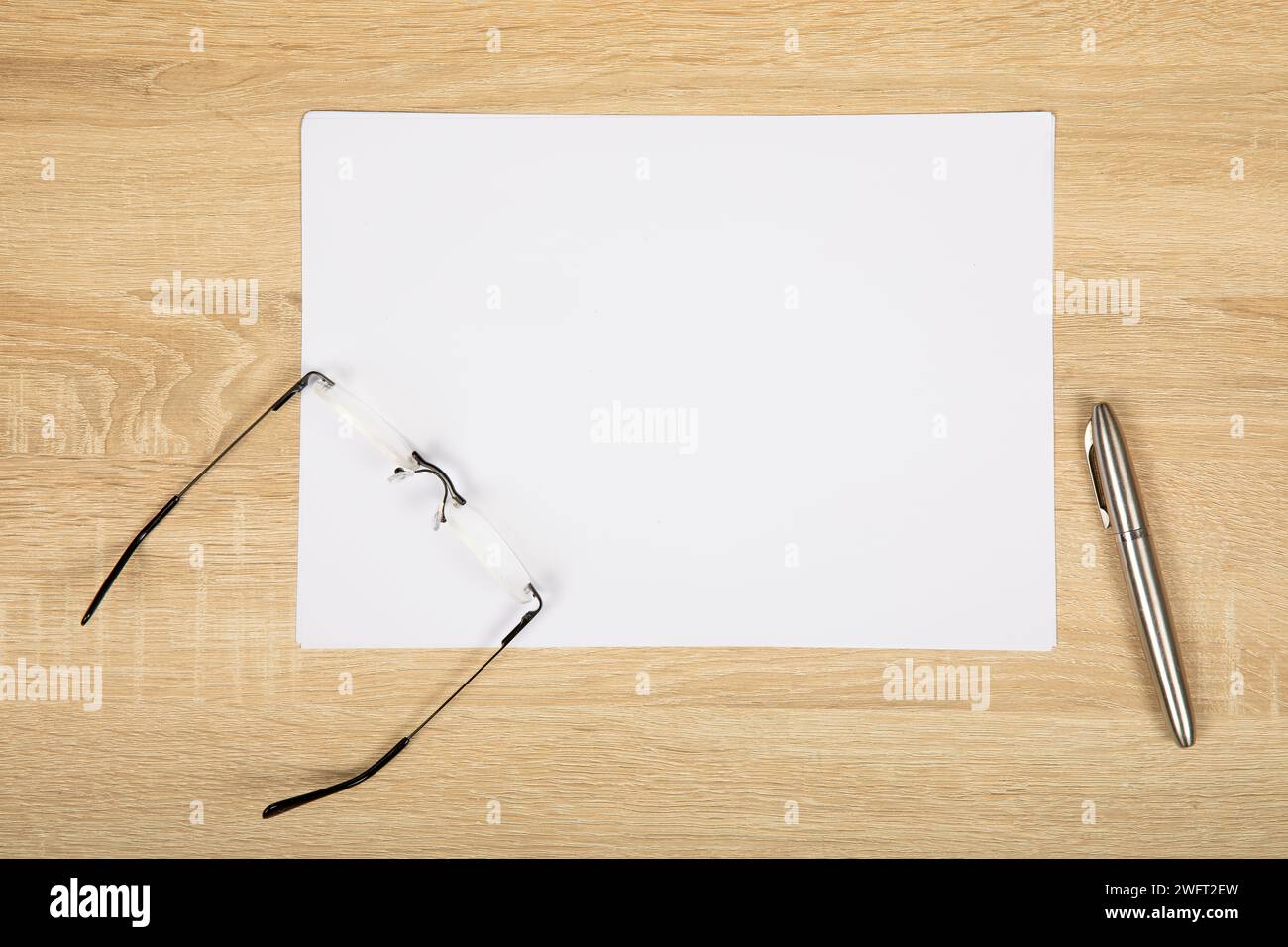 Moderner minimalistischer Arbeitsbereich: Weißpapier, Lesebrille und Silbermarker auf Holztisch. Stockfoto
