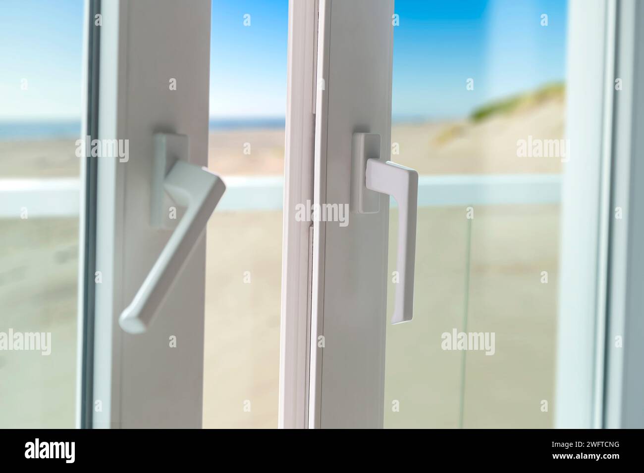 Schiebetür vom Balkon zum Strand. Nahaufnahme des Türschlosses mit schöner und sonniger Meereslandschaft im Hintergrund. Weiße PVC-Tür und Sicherheitsglas. Stockfoto
