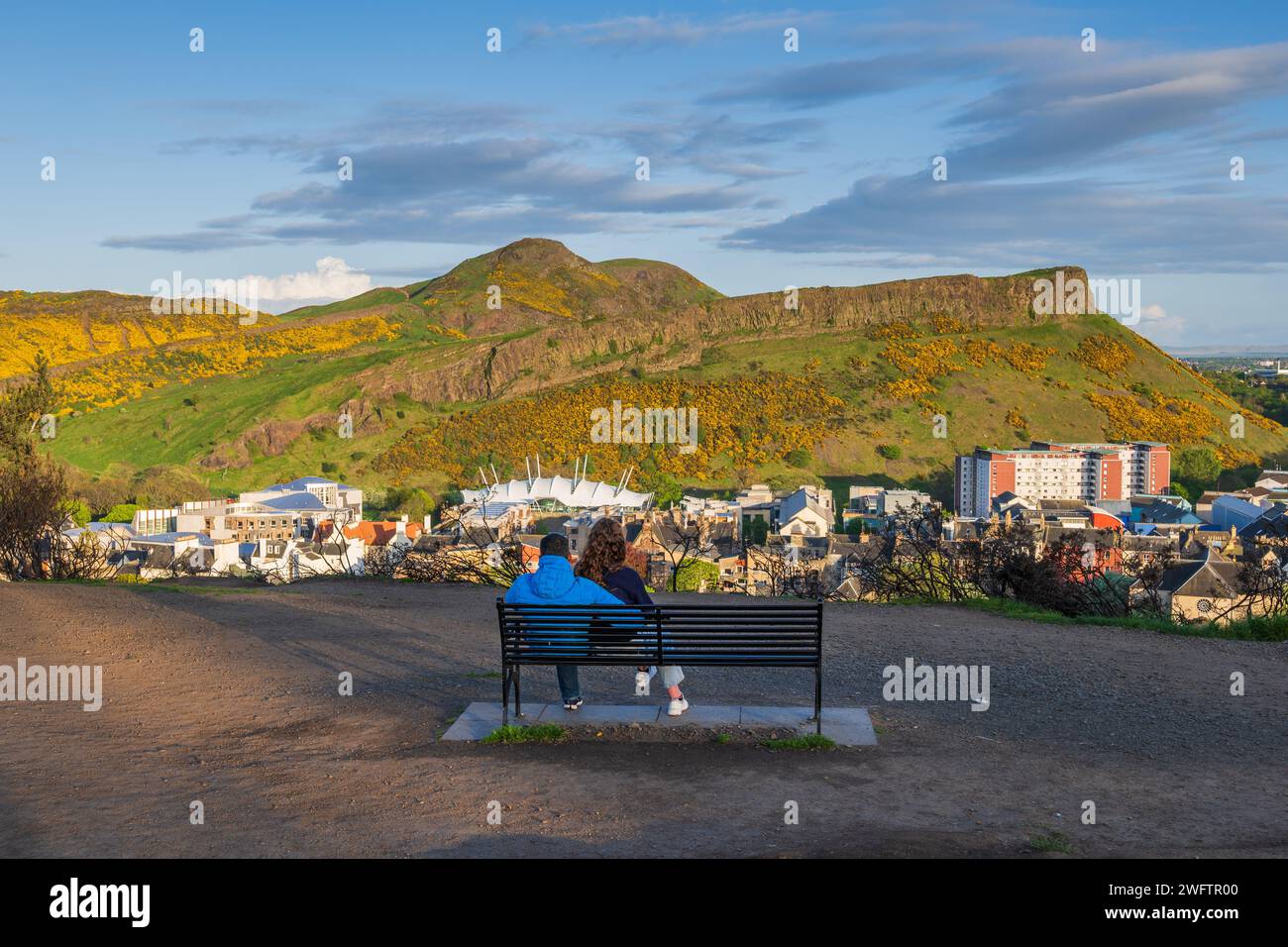 Einsames Paar auf einer Bank auf dem Calton Hill mit Blick auf den Holyrood Park mit Arthurs Sitz bei Sonnenuntergang in Edinburgh, Schottland, Großbritannien. Stockfoto