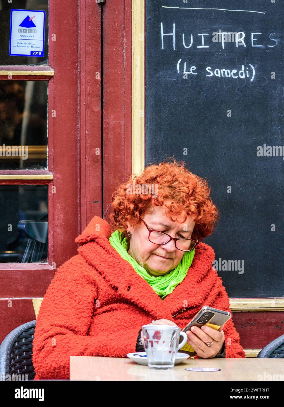 Frau mit Ingwer-/O-Range-Haaren saß am Gesichtstisch und schaute auf das Smartphone - Tours, Indre-et-Loire (37), Frankreich. Stockfoto