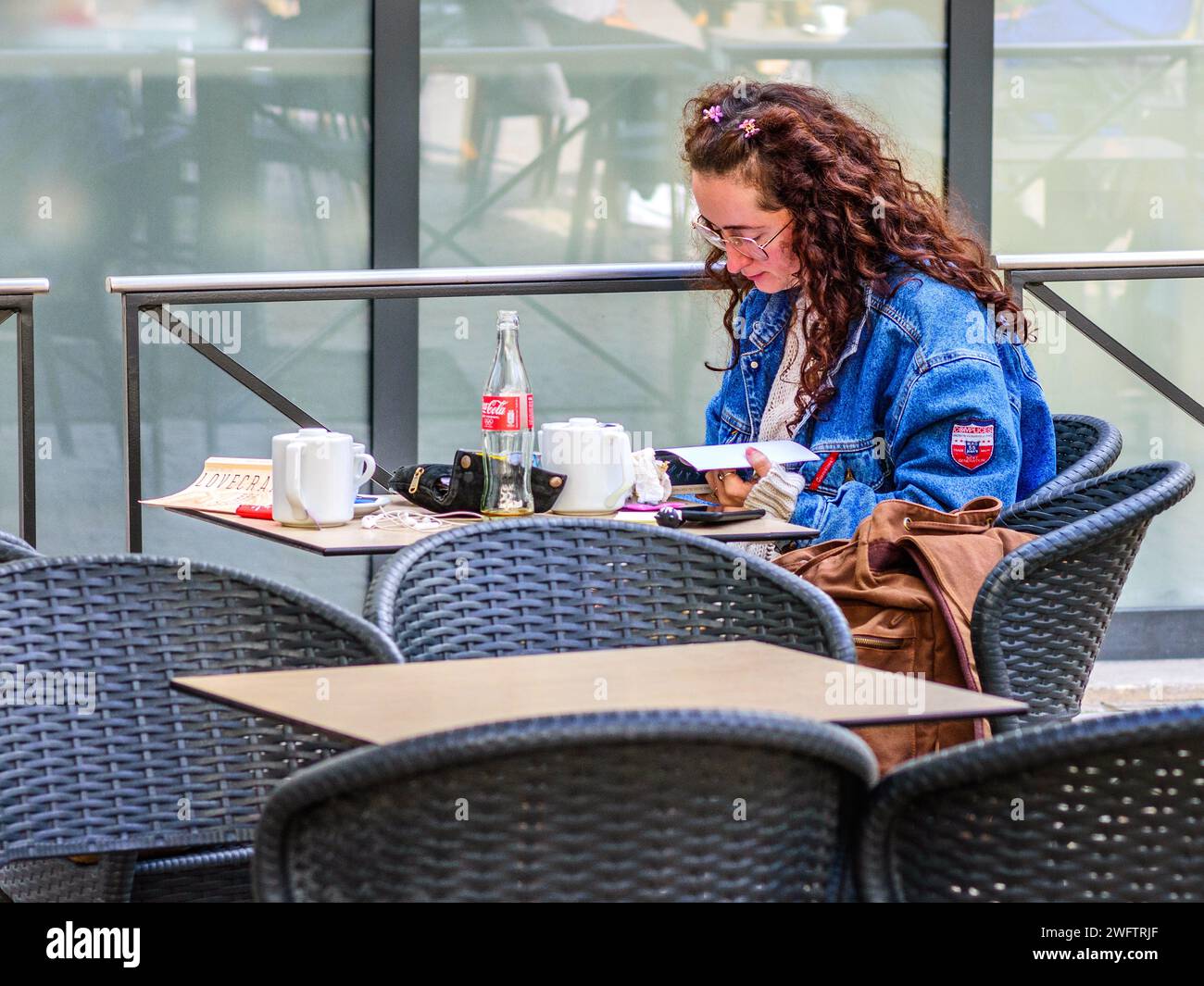 Junge Frau mit langen welligen dunkelbraunen Haaren liest am Kaffeetisch - Tours, Indre-et-Loire (37), Frankreich. Stockfoto