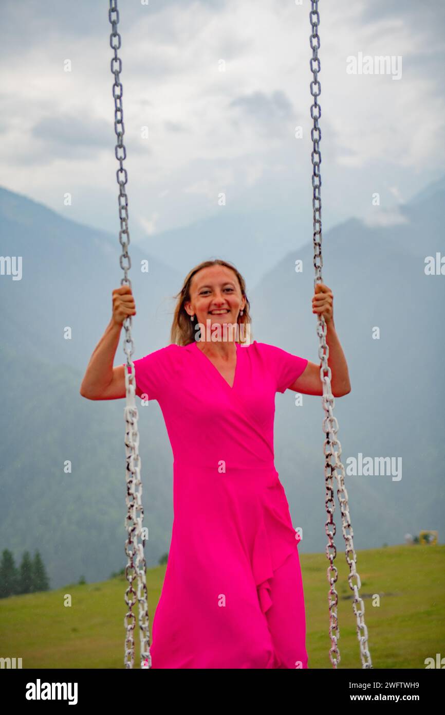 Flüsternde Winde und schwingende Freuden eines Mädchens in einem rosa Kleid auf einer Schaukel Stockfoto