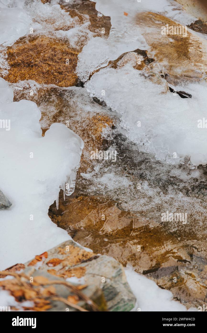 Schmelzendes Eis umgibt eine massive Steinplatte inmitten eines fließenden Flusses Stockfoto